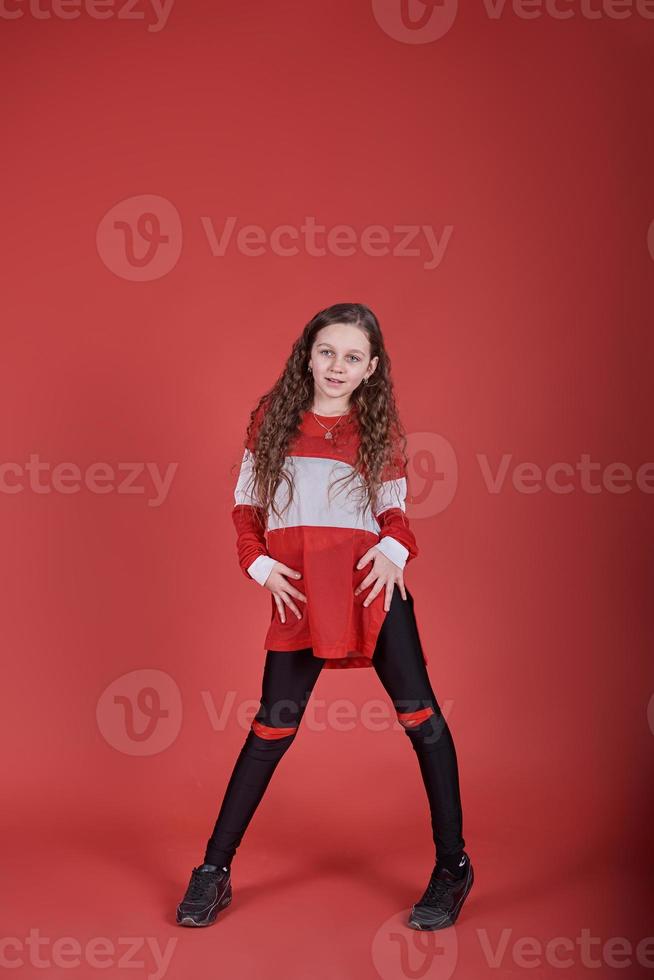 Young urban woman dancing on red background, modern slim hip-hop style teenage girl photo