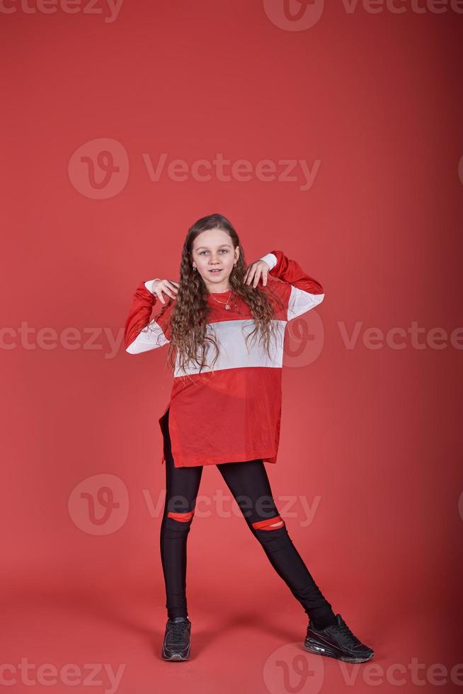 Joven hermosa linda chica bailando sobre fondo rojo, moderno y delgado estilo hip-hop adolescente saltando foto