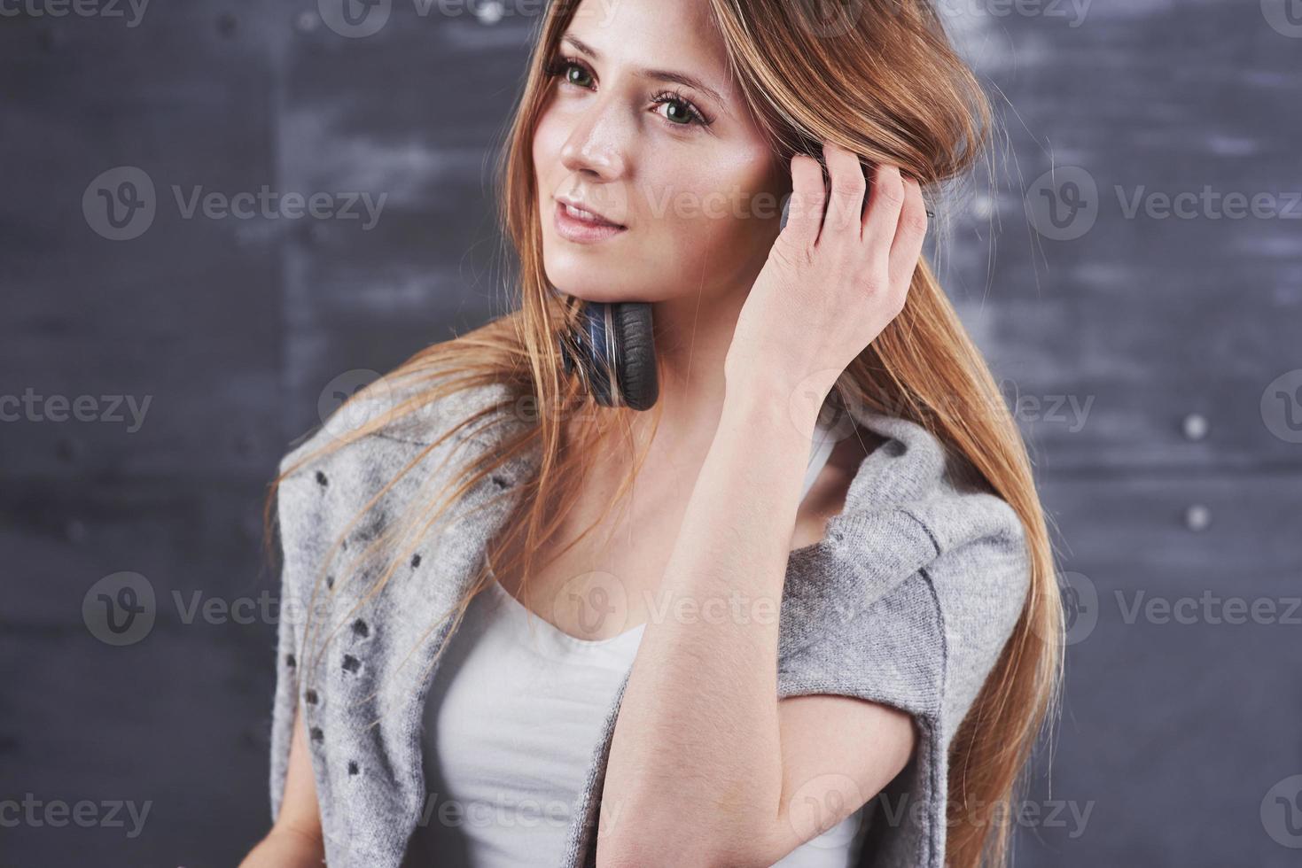 Disparo en la cabeza de la joven mujer rubia adorable con linda sonrisa vistiendo grandes auriculares de monitoreo profesional negro contra el fondo gris del estudio foto