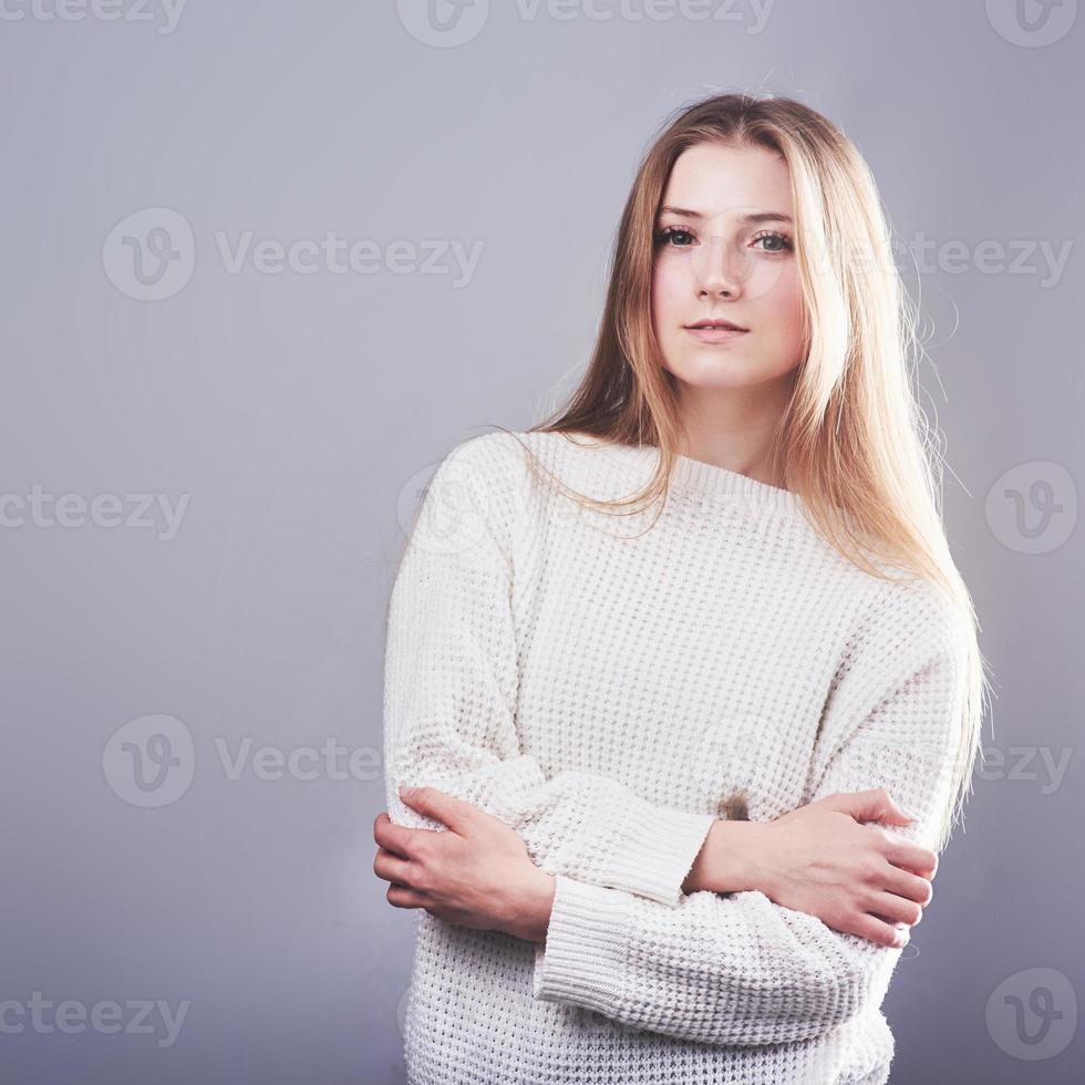 Portrait of beautiful young woman in white sweater and jeans, isolated on gray background photo