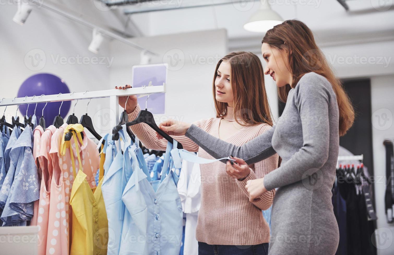 deberíamos mirar los vestidos nuevos vista trasera de dos hermosas mujeres con bolsas de compras mirando hacia otro lado con una sonrisa mientras caminamos en la tienda de ropa foto