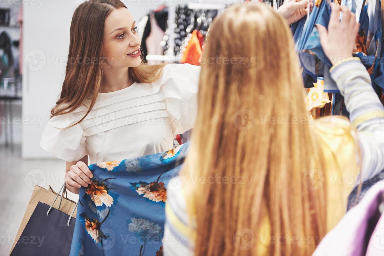 deberíamos mirar los vestidos nuevos vista trasera de dos hermosas mujeres con bolsas de compras mirando hacia otro lado con una sonrisa mientras caminamos en la tienda de ropa foto