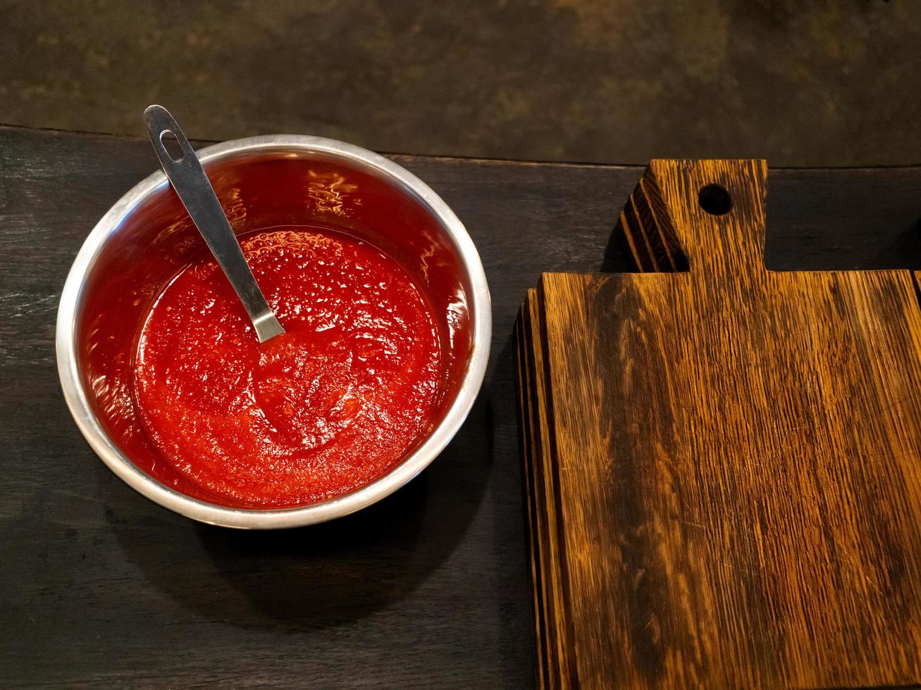 salsa de tomate en un recipiente sobre una mesa oscura cerca de una tabla de cortar de madera foto