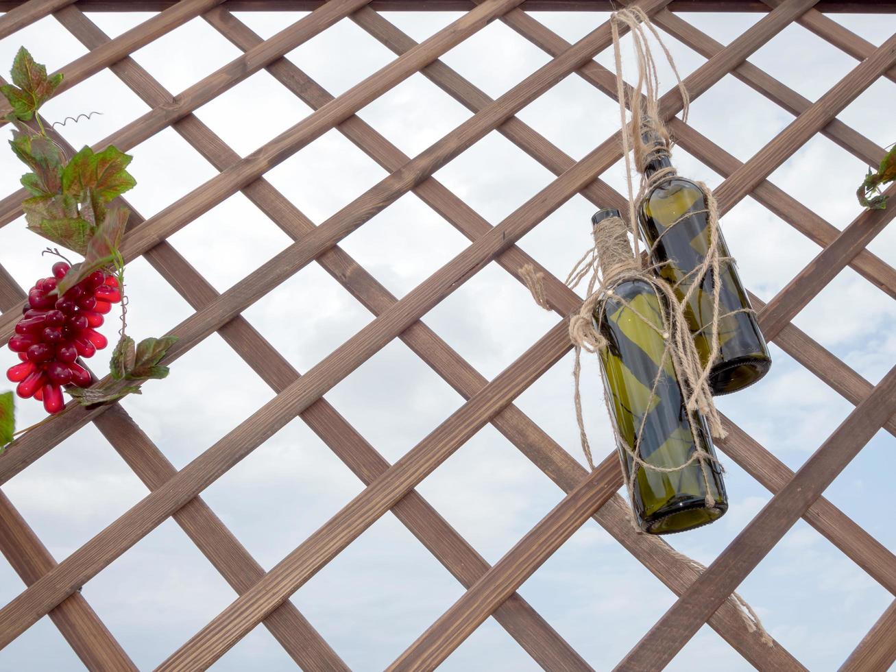 Two empty wine bottles hanging on a decorative lattice photo