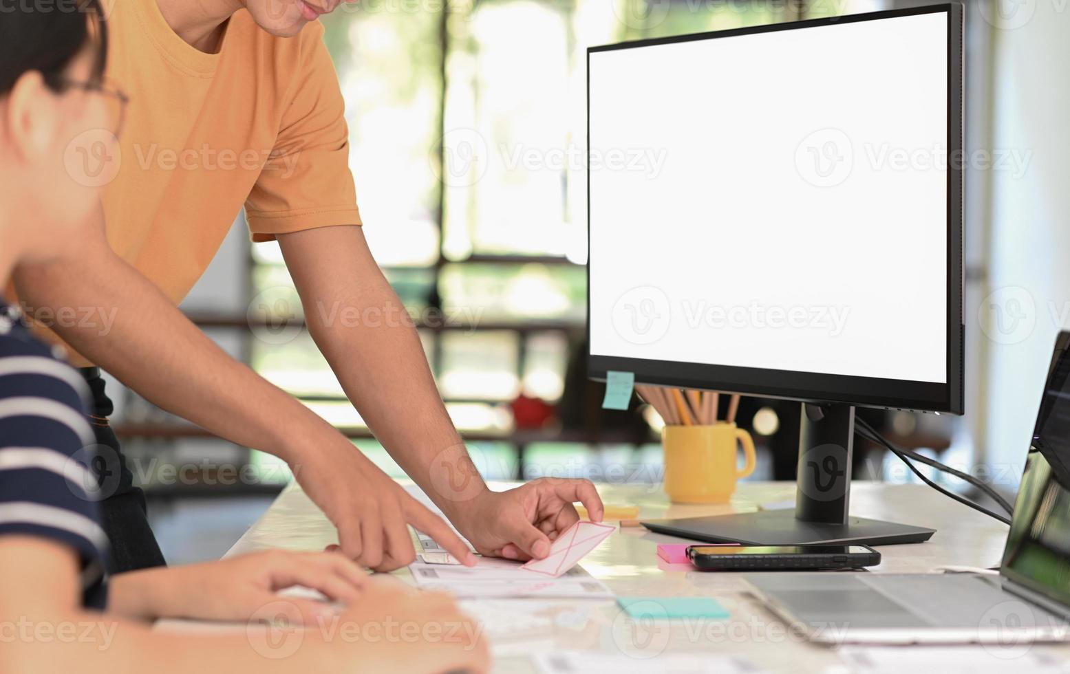 A team of smartphone app designers collaborated to design a new project with a mockup computer blank screen. photo