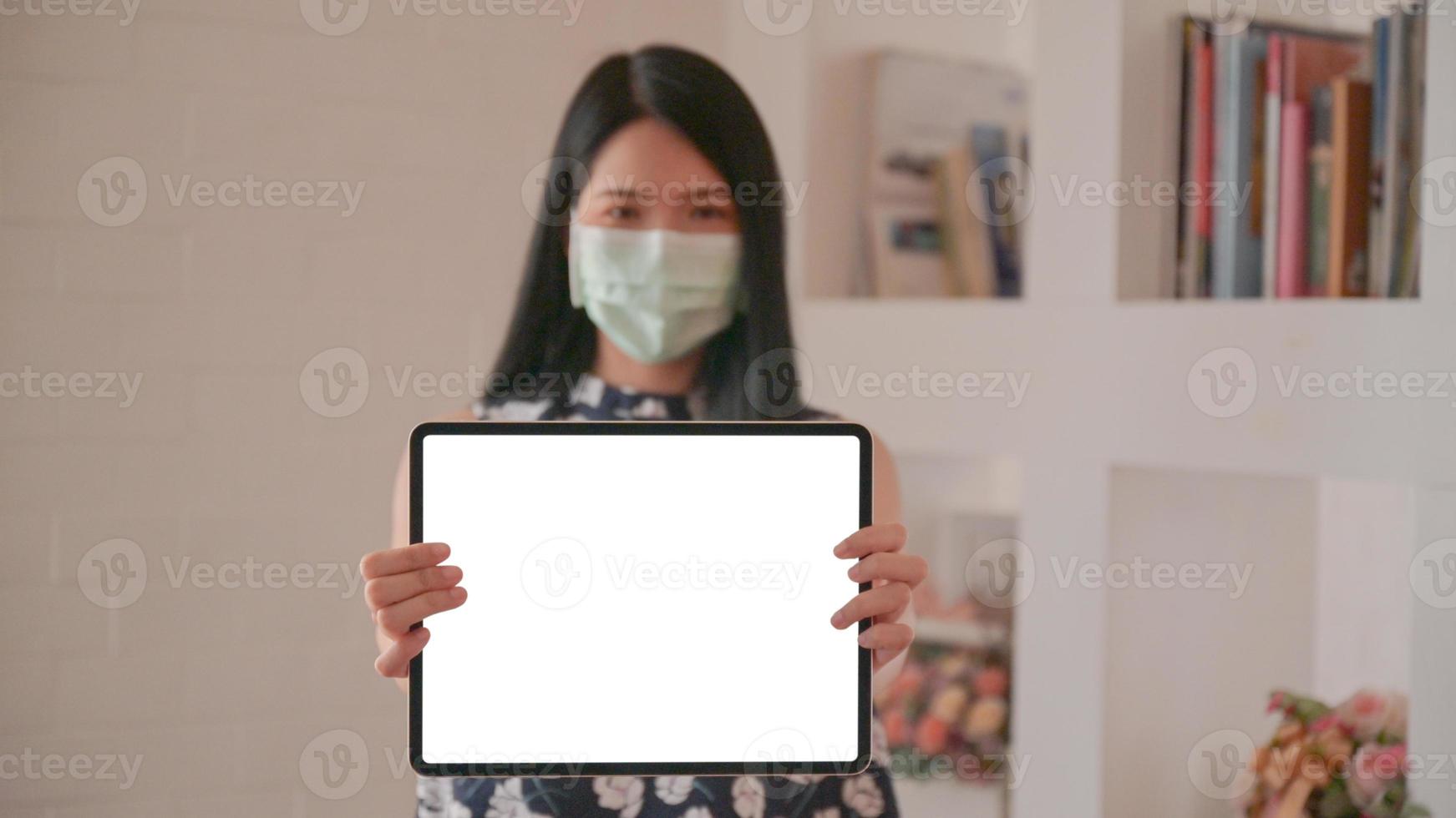 Asian woman wearing a mask holding a tablet facing the front screen for a message to protect against Corona virus or Covid-19. photo
