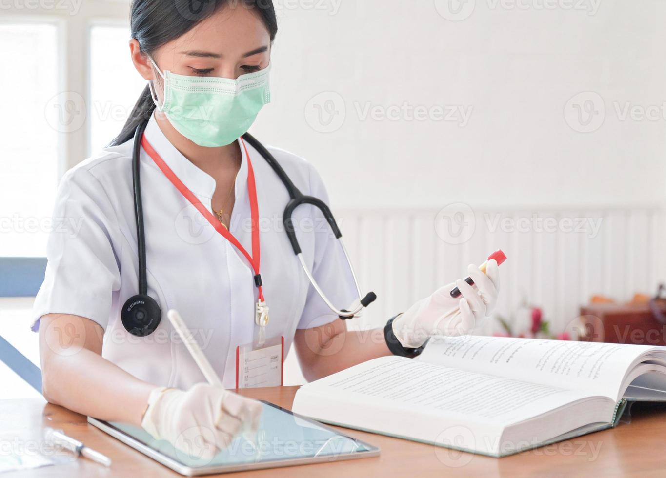 el médico está buscando en el historial del paciente para comparar los resultados de los tubos de análisis de sangre con una tableta. foto