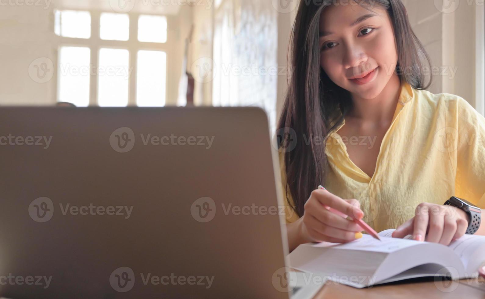 Asian teenage female student search for information from laptop and take notes. She prepares for university entrance exam. photo
