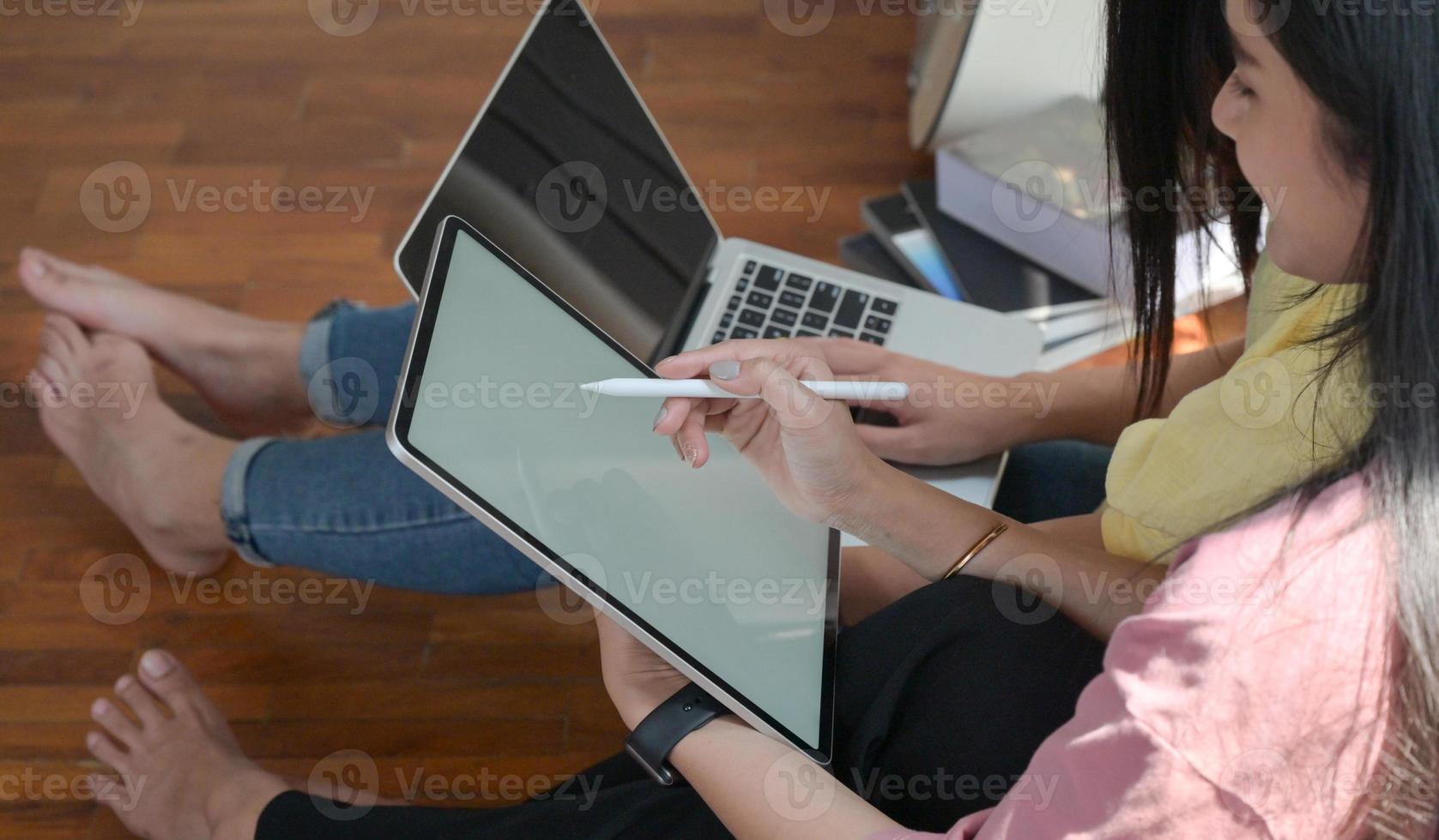 Two female college students use a tablet and a laptop to study online at home to prevent the Covid-19 virus outbreak. photo