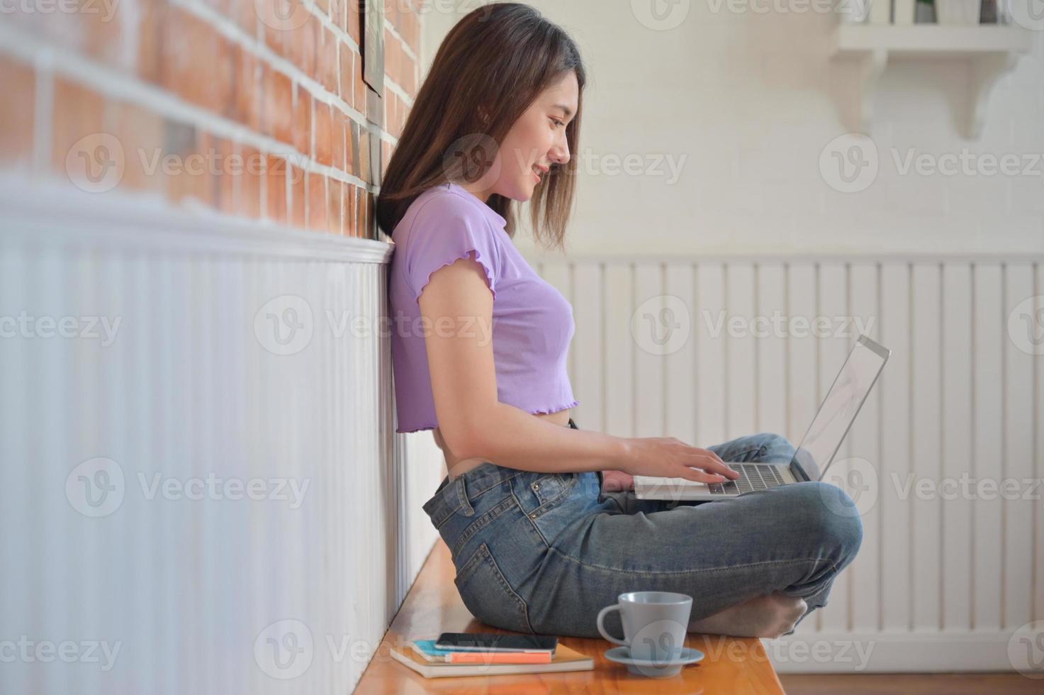 joven estudiante sentada cómodamente está usando una computadora portátil para hacer videollamadas con amigos en casa. foto