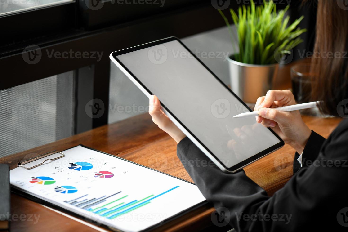 Cropped shot of a female employee using a pen to write on a tablet and graph documents on the table. photo