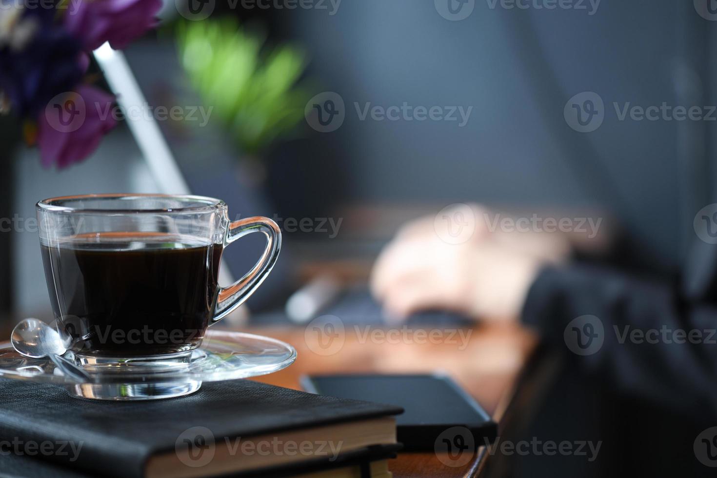 maqueta de café en el escritorio con el personal está usando una computadora portátil en la oficina detrás. foto