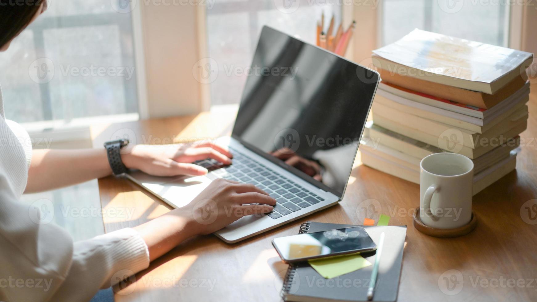 De cerca, la mano de la joven está usando una computadora portátil en un escritorio de madera en la oficina con una hermosa iluminación. foto