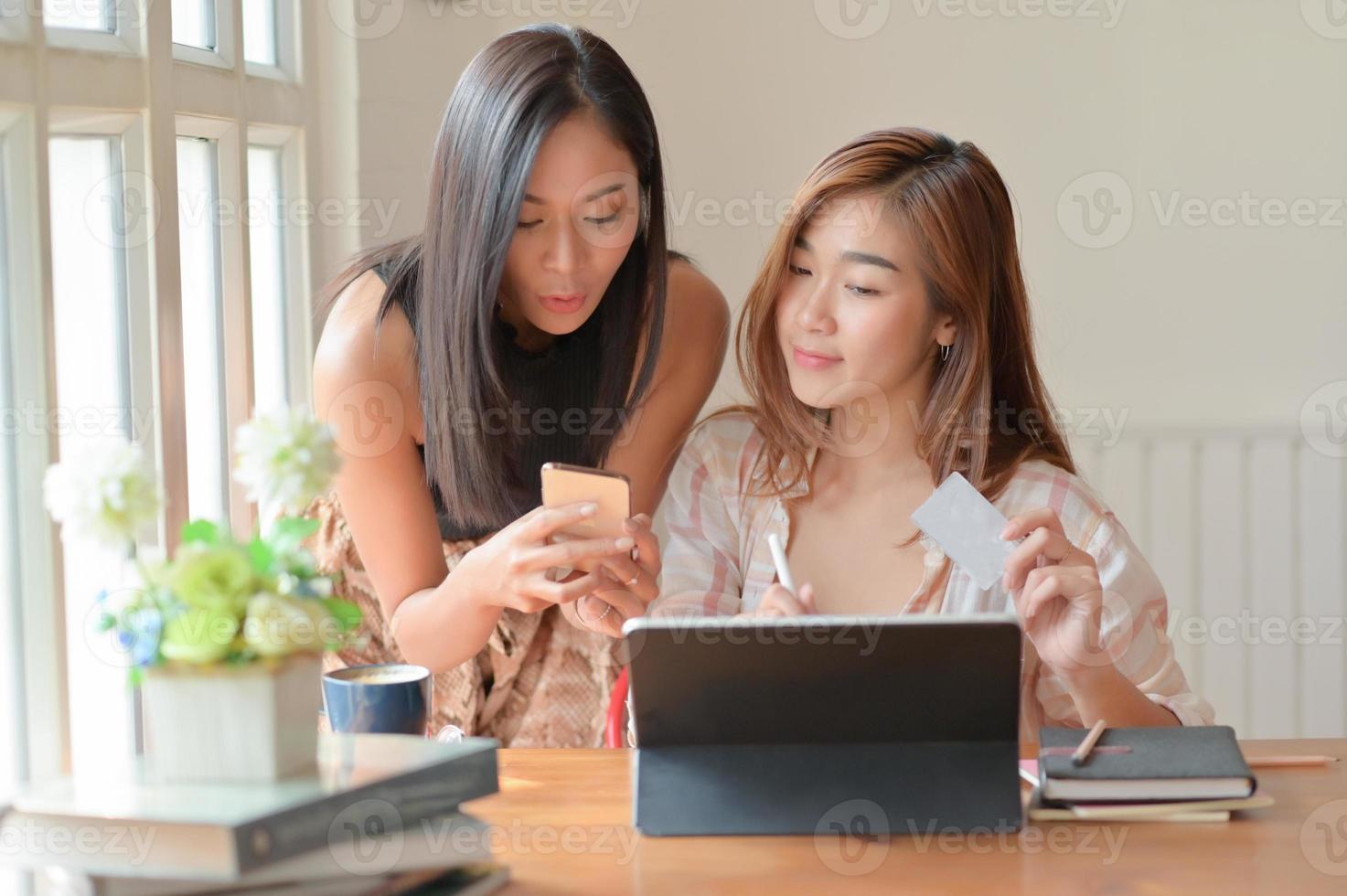 Two Asian women hold a credit card and use a smartphone to search for shopping information. photo