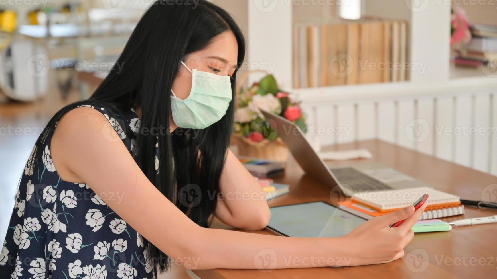 Woman wearing a mask is using a smartphone in a cafe.She is at risk of being infected with the Covid-19 virus. photo