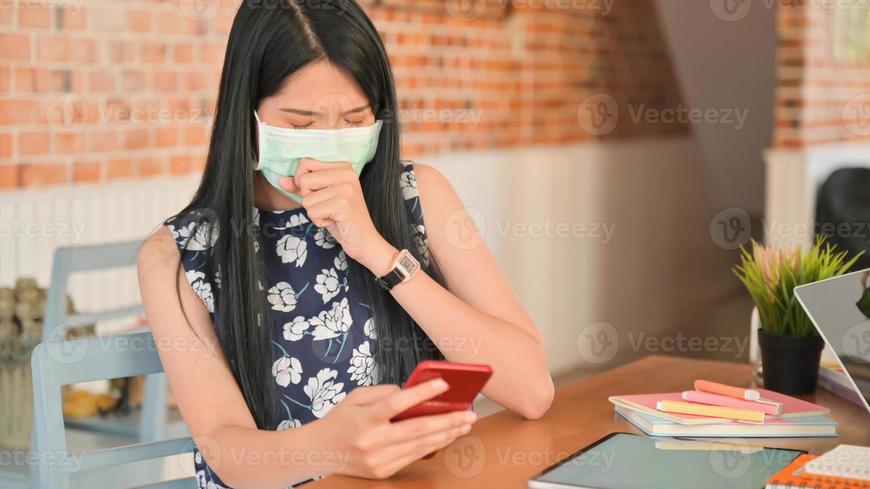 Una mujer que usa una máscara está usando un teléfono inteligente en un café y está en riesgo de infectarse con el virus covid-19. foto