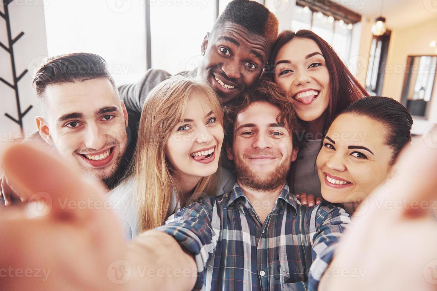 Self portrait of mixed race unity of african, american, asian, caucasian friends, happy bearded men and beautiful women in red santa hat showing thumb up, like, ok gesture to the camera in office photo