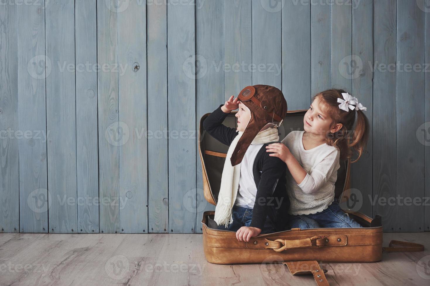 Happy kid in pilot hat and little girl playing with old suitcase. Childhood. Fantasy, imagination. Travel concept photo
