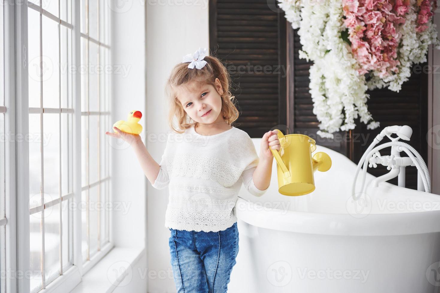 Funny little baby girl with curly hair. Get ready to take a bath. Spacious lighted bathroom. The concept of a healthy and clean body. Caring for yourself since childhood photo