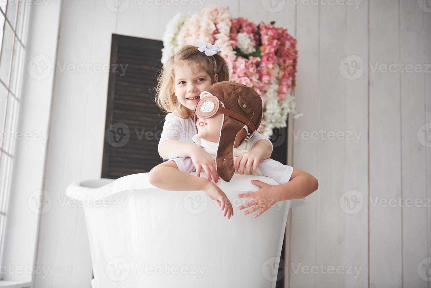 retrato de una niña y un niño con sombrero de piloto jugando en el baño a los pilotos o marineros. el concepto de viaje, infancia y realización de sueños foto