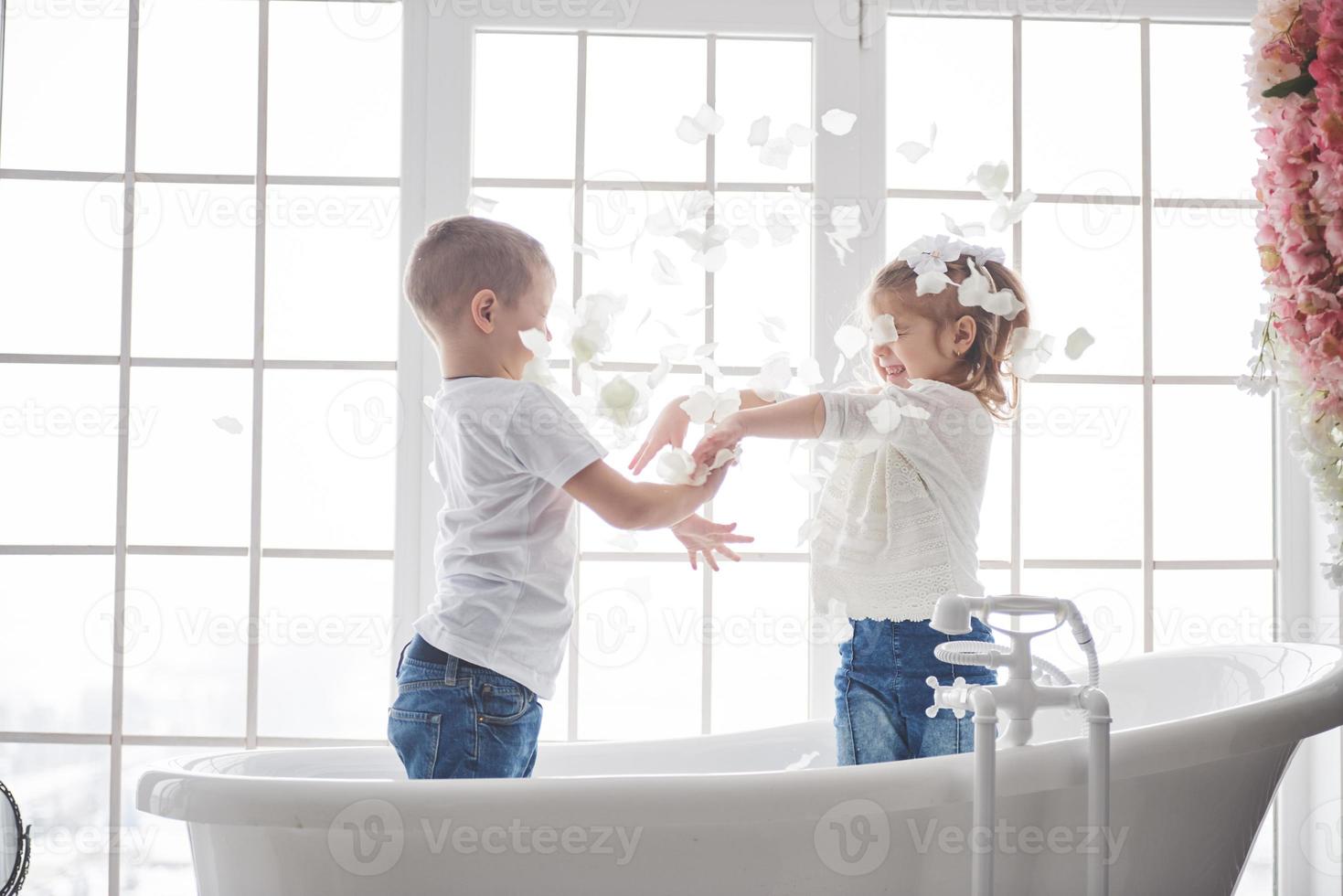 niño jugando con pétalos de rosa en el baño de su casa. niña y niño adulando diversión y alegría juntos. el concepto de infancia y la realización de sueños, fantasía, imaginación foto