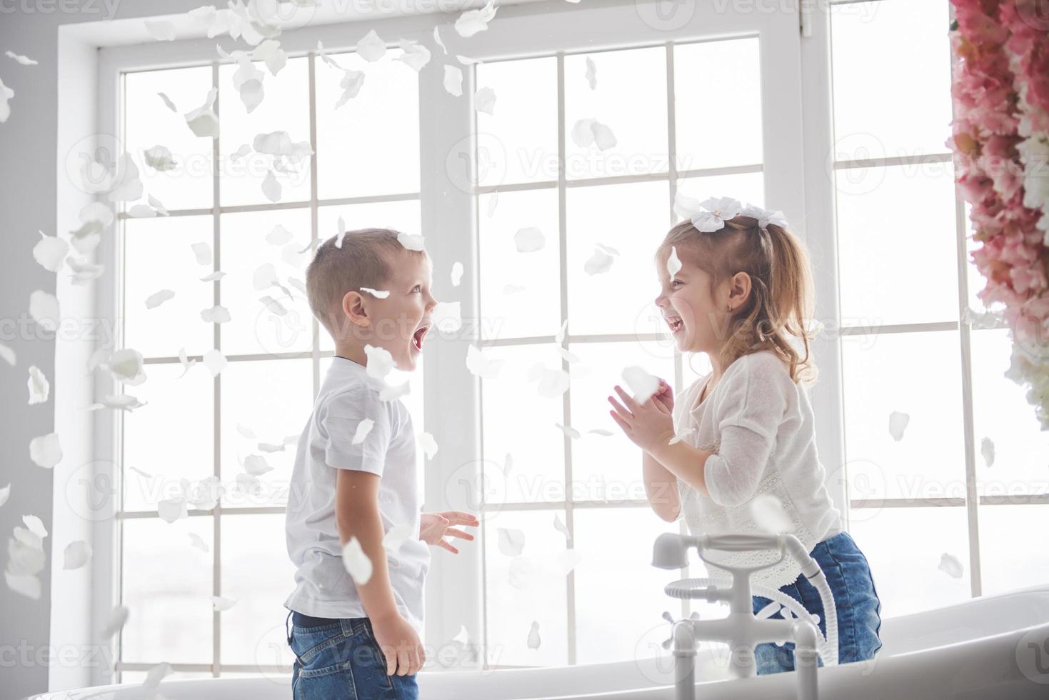 niño jugando con pétalos de rosa en el baño de su casa. niña y niño adulando diversión y alegría juntos. el concepto de infancia y la realización de sueños, fantasía, imaginación foto