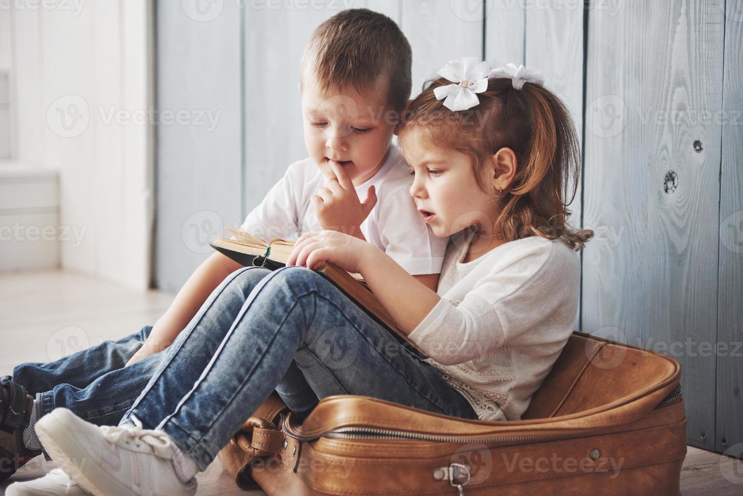 Ready to big travel. Happy little girl and boy reading interesting book carrying a big briefcase and smiling. Travel, freedom and imagination concept photo