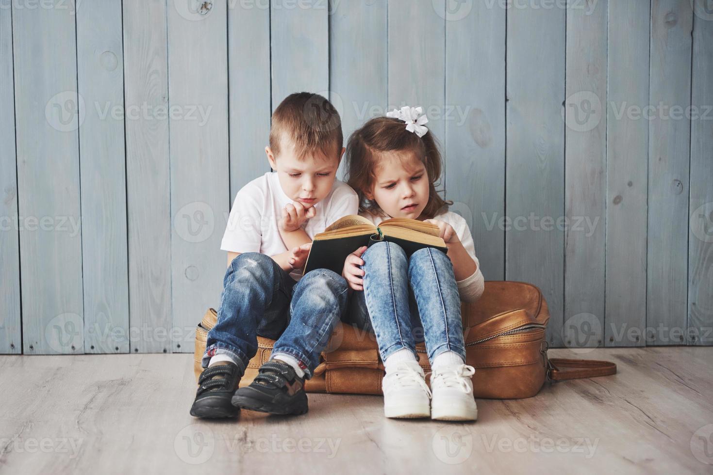 listo para grandes viajes. feliz niña y niño leyendo un libro interesante con un maletín grande y sonriendo. concepto de viaje, libertad e imaginación. foto