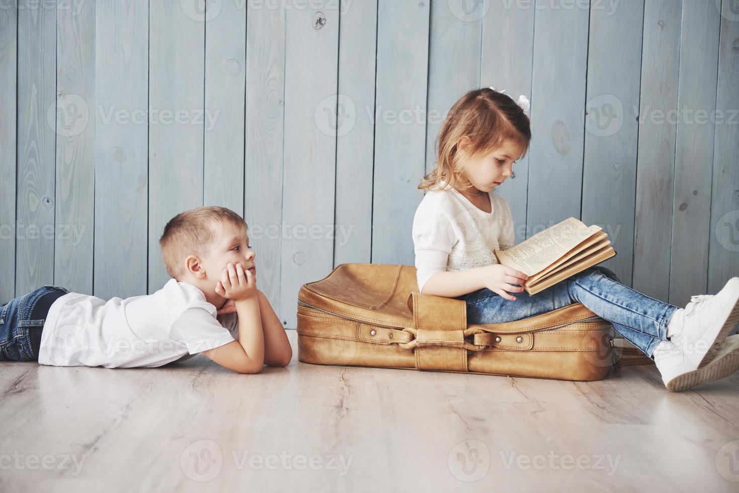 listo para grandes viajes. feliz niña y niño leyendo un libro interesante con un maletín grande y sonriendo. concepto de viaje, libertad e imaginación. foto