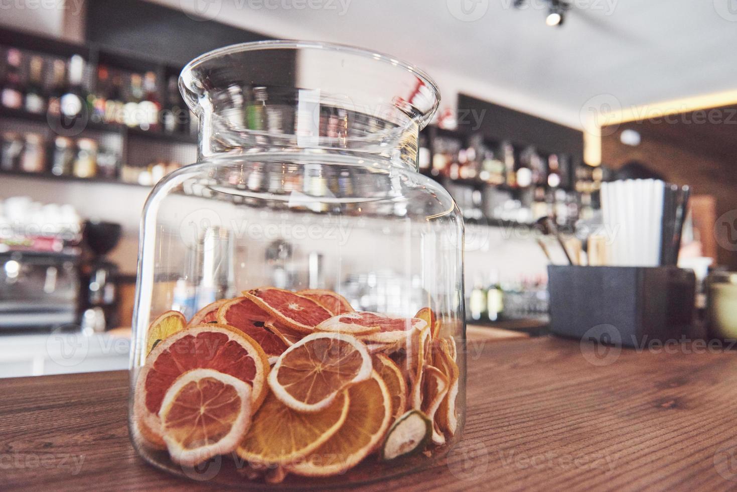 Ruedas de naranja, lima y limón confitadas secas en un recipiente de vidrio grande con el contenido también dispuesto en un bloque de carnicero alrededor de un frasco con azúcar sin refinar y tapa de metal foto