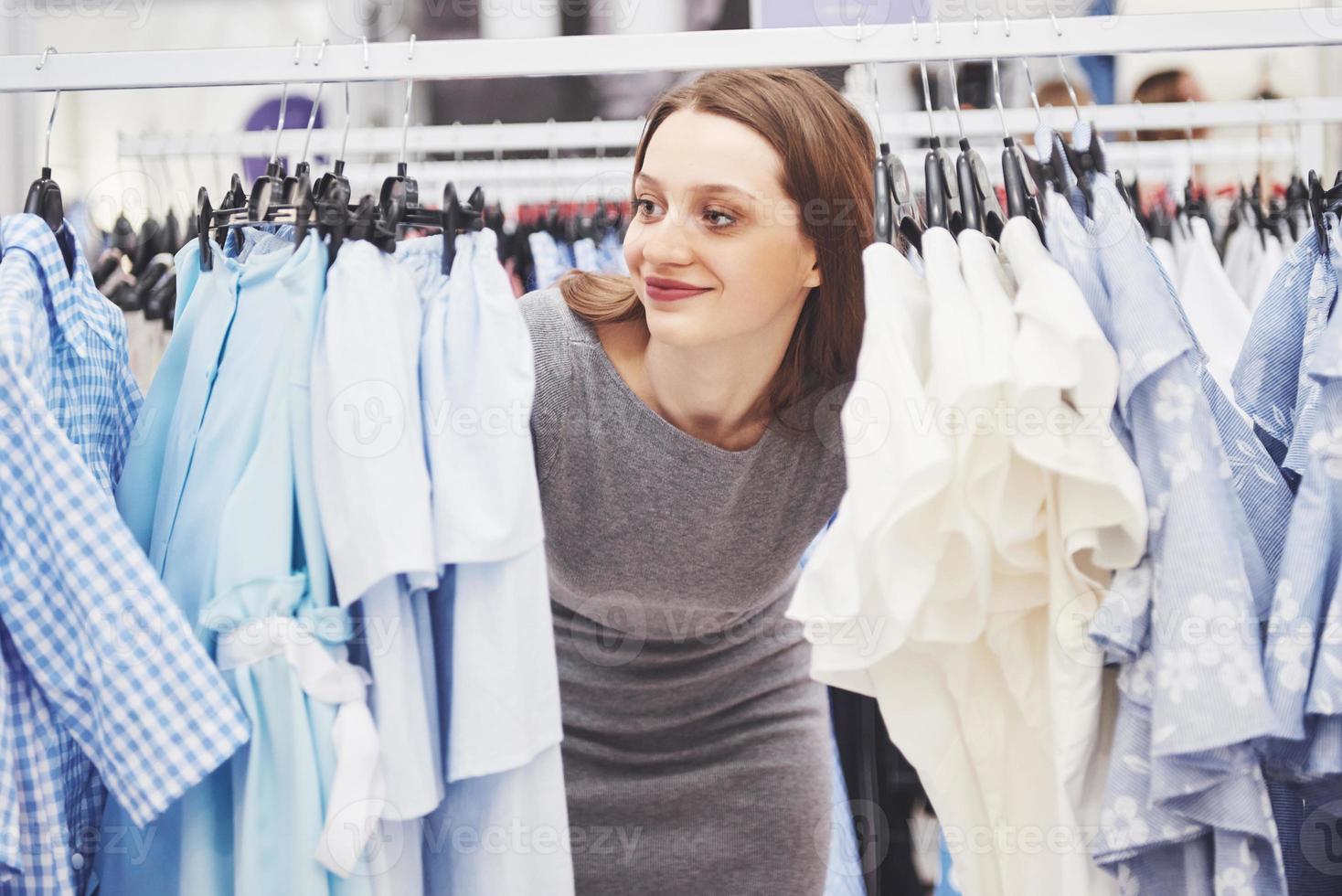 concepto de venta, moda, consumismo y personas - mujer joven feliz con bolsas de compras eligiendo ropa en el centro comercial o tienda de ropa foto