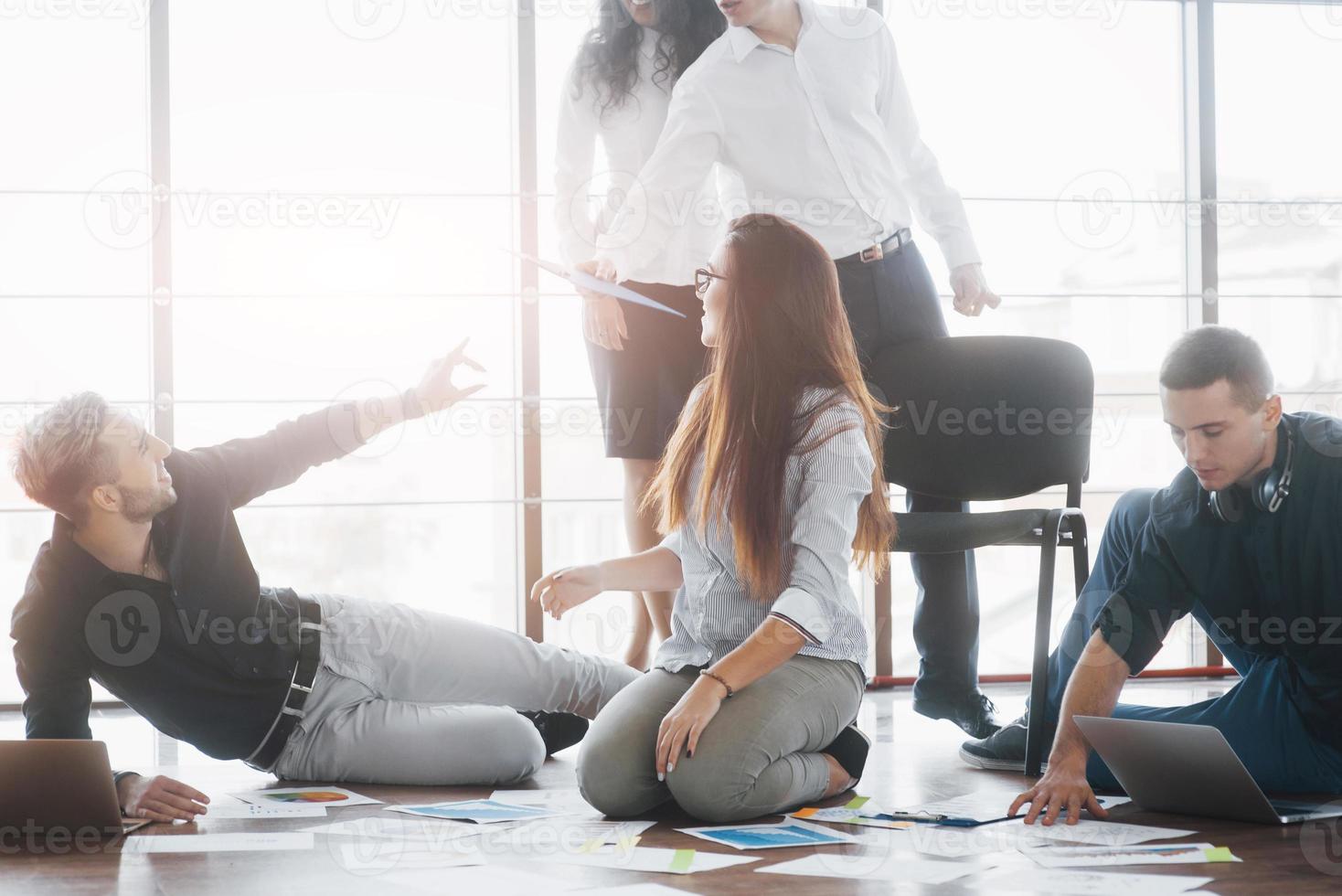 Planning strategy together. Business team looking at papers on floor with manager pointing to one idea. Cooperation corporate achievement. Planning design draw. Teamwork concept photo