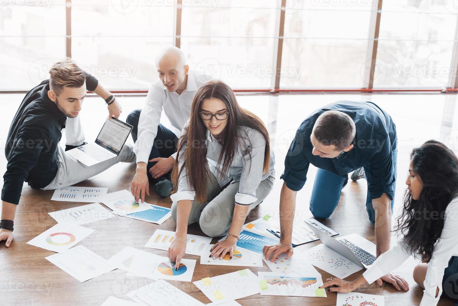 Planning strategy together. Business team looking at papers on floor with manager pointing to one idea. Cooperation corporate achievement. Planning design draw. Teamwork concept photo