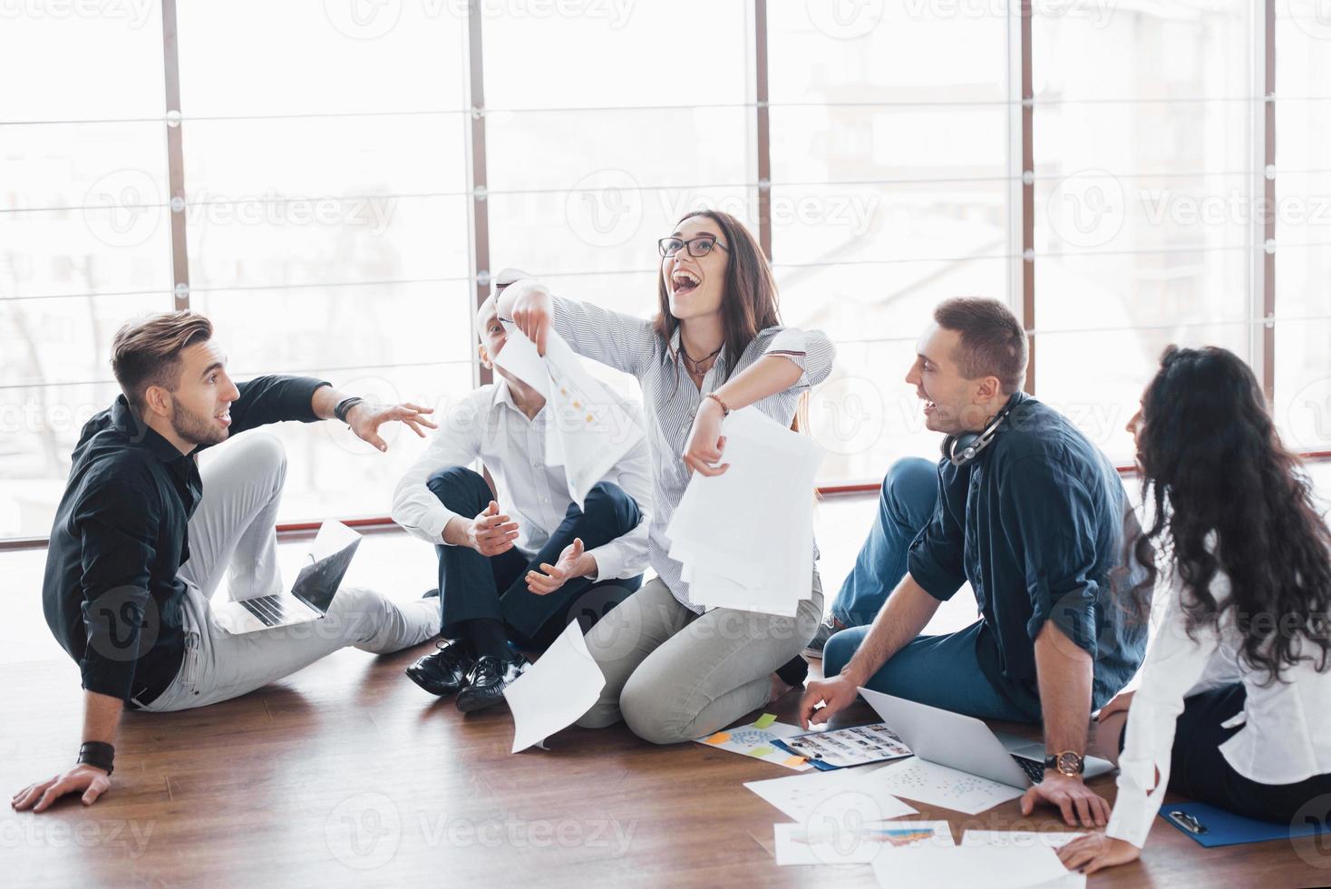 Young creative people in modern office. Group of young business people are working together with laptop. Freelancers sitting on the floor. Cooperation corporate achievement. Teamwork concept photo