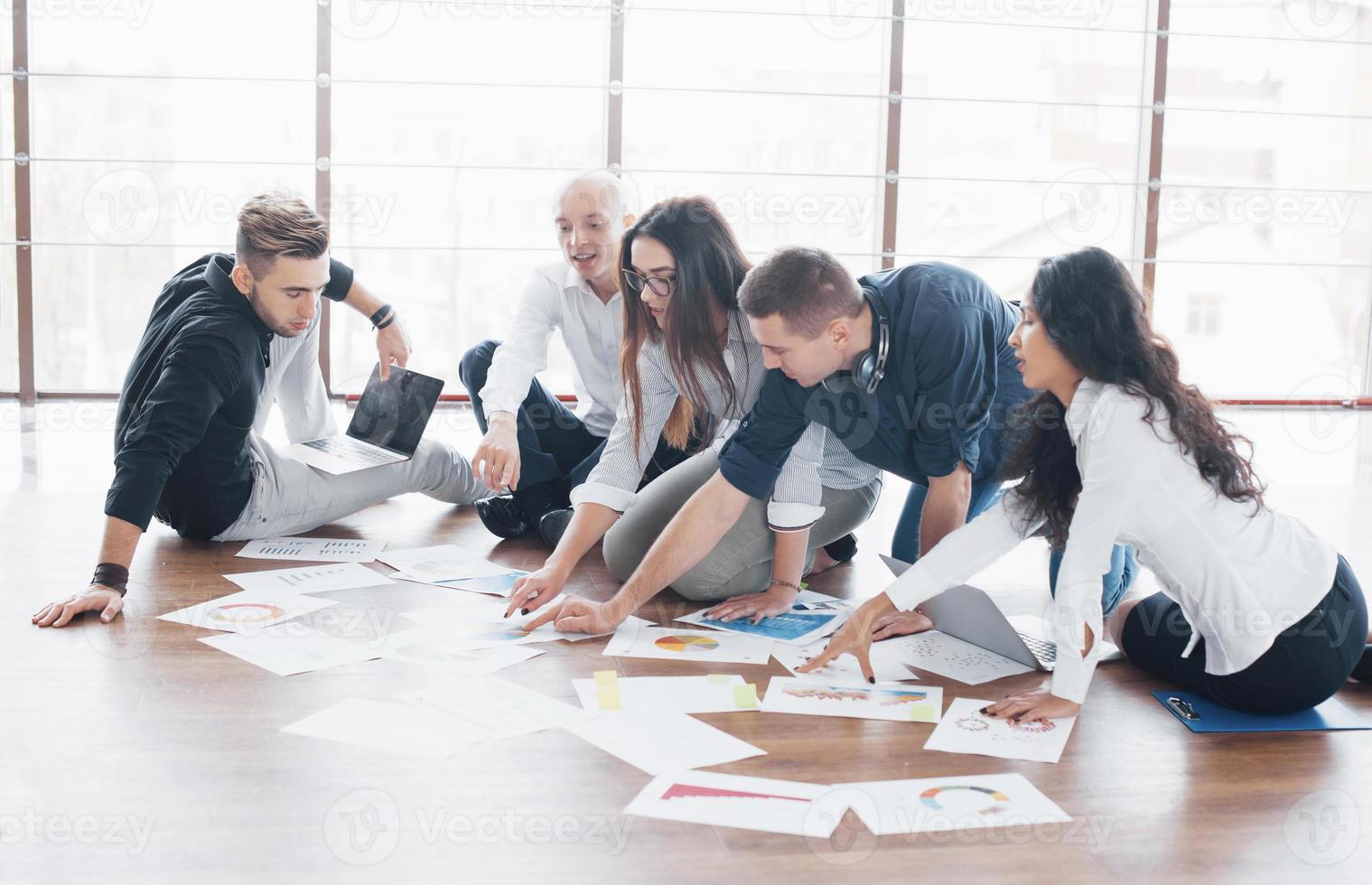 Young creative people in modern office. Group of young business people are working together with laptop. Freelancers sitting on the floor. Cooperation corporate achievement. Teamwork concept photo