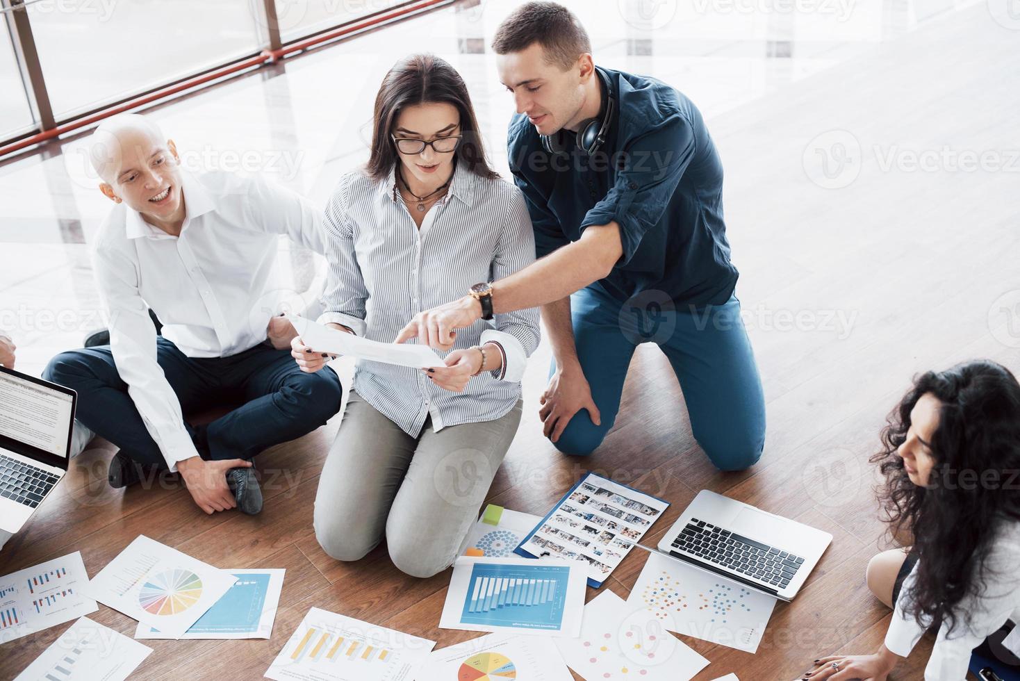 Planning strategy together. Business team looking at papers on floor with manager pointing to one idea. Cooperation corporate achievement. Planning design draw. Teamwork concept photo