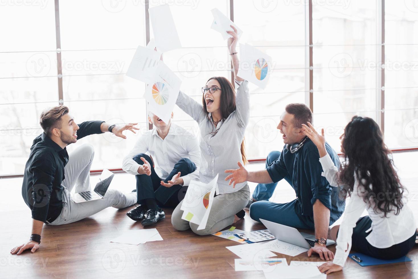 Young creative people in modern office. Group of young business people are working together with laptop. Freelancers sitting on the floor. Cooperation corporate achievement. Teamwork concept photo