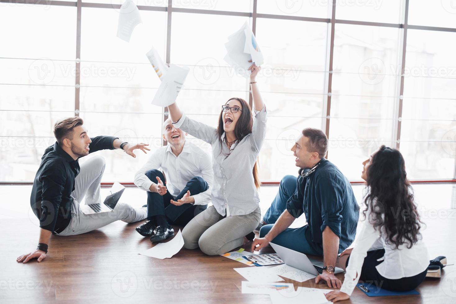 jóvenes creativos en la oficina moderna. grupo de jóvenes empresarios están trabajando junto con la computadora portátil. autónomos sentados en el suelo. logro corporativo de cooperación. concepto de trabajo en equipo foto