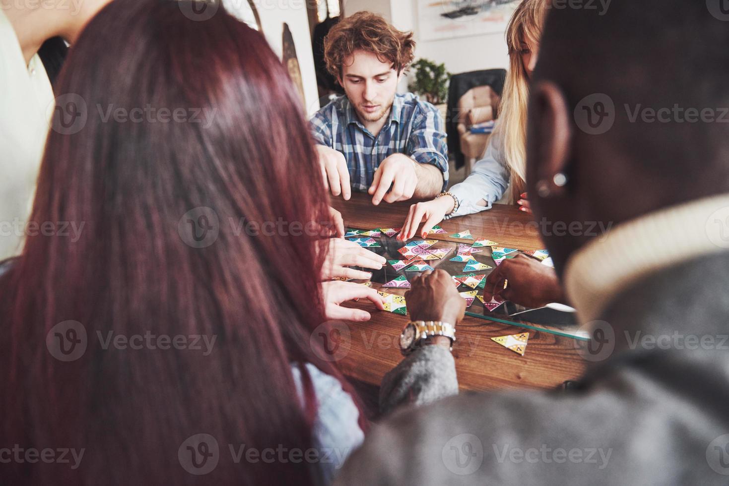 grupo de amigos creativos sentados en la mesa de madera. gente divirtiéndose mientras juega al juego de mesa. foto