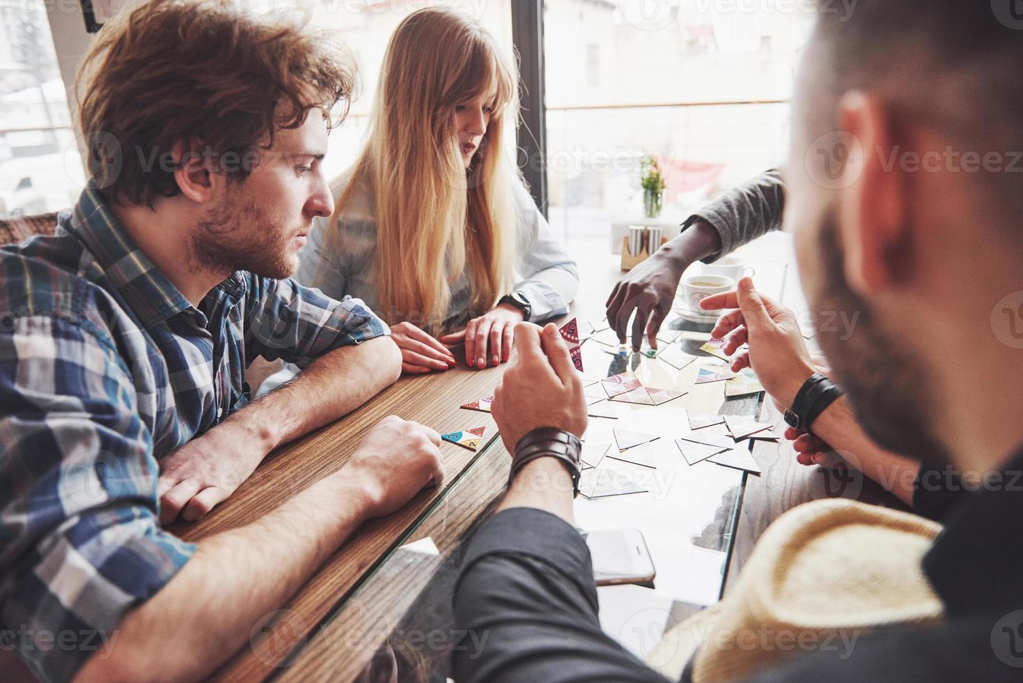 Group of creative multietnic friends sitting at wooden table. People having fun while playing board game photo