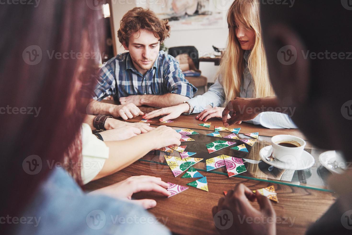 Group of creative friends sitting at wooden table. People having fun while playing board game photo