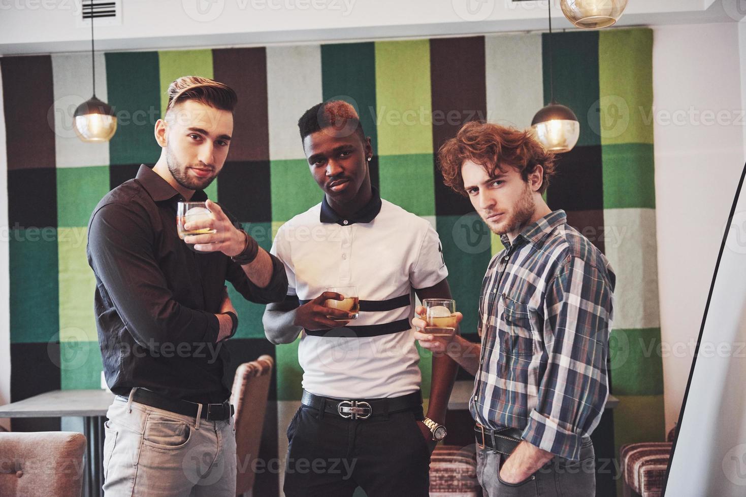 Prometedores jóvenes multiétnicos celebrando y bebiendo tostadas de whisky, reloj gadget foto