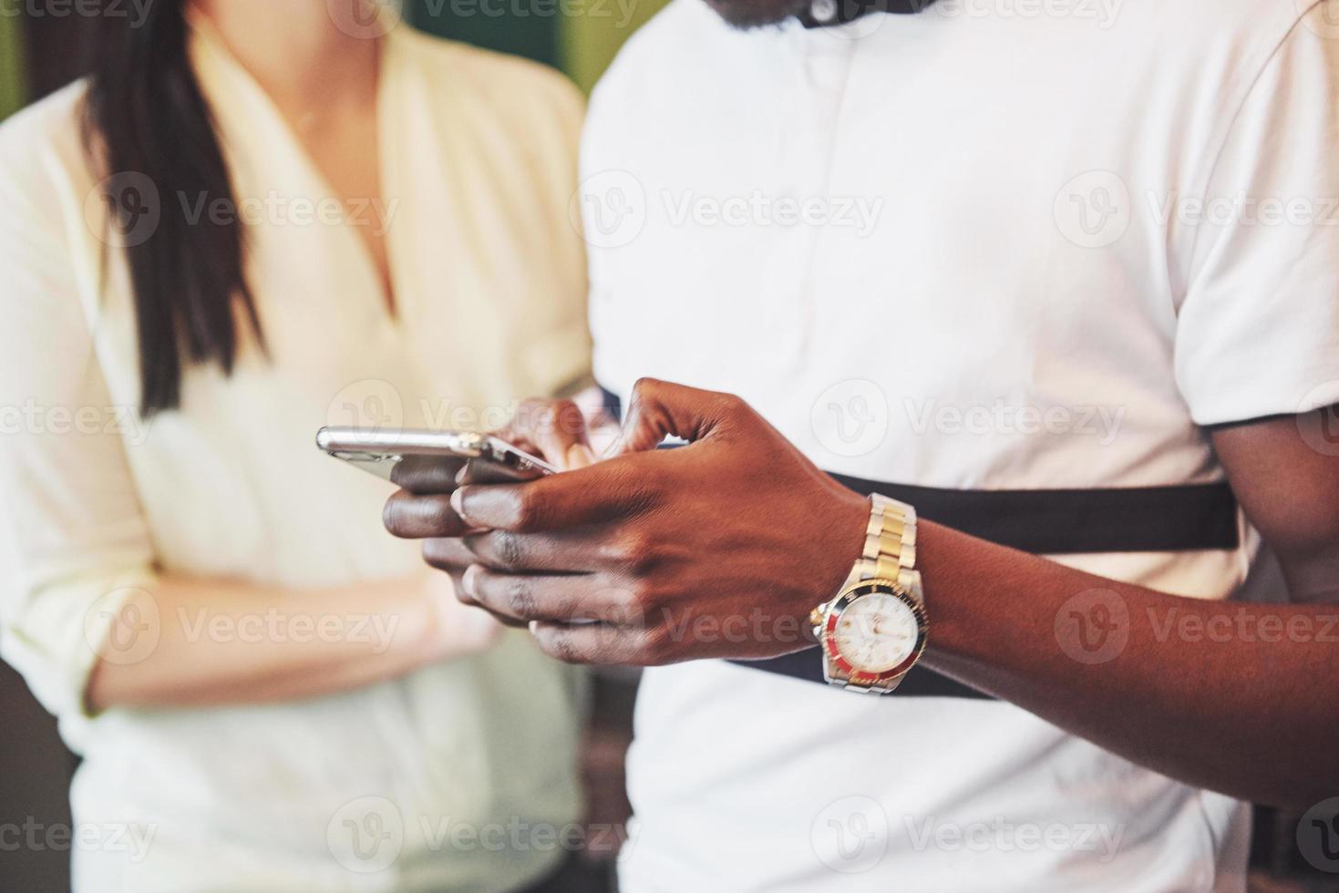Cerrar jóvenes amigos mirando el teléfono inteligente mientras está sentado en la cafetería. Personas de raza mixta en restaurante mediante teléfono móvil. foto