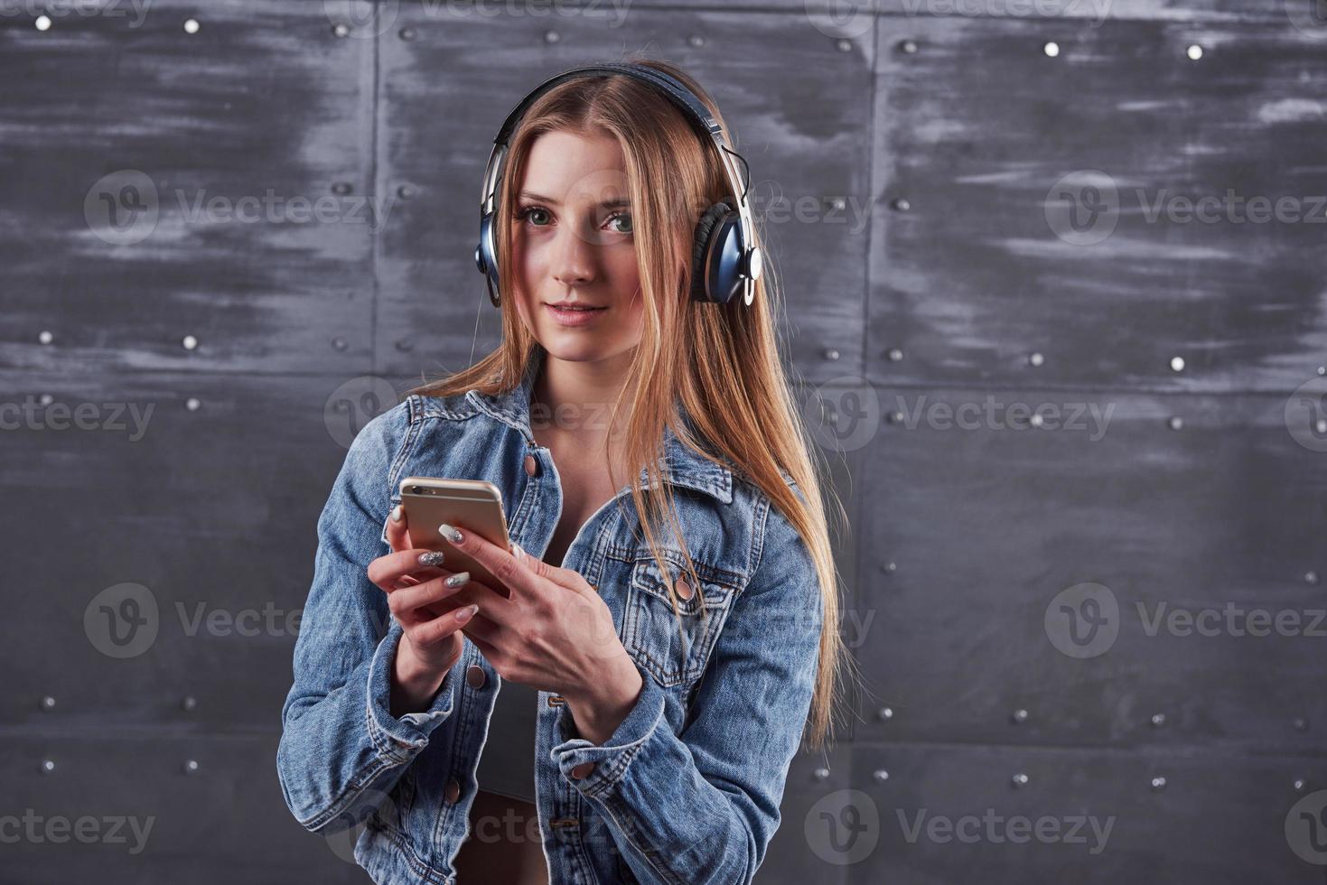 moda, ropa, concepto de personas. atractiva joven sexy con chaqueta de jeans. chica está posando en el estudio escucha música en auriculares foto