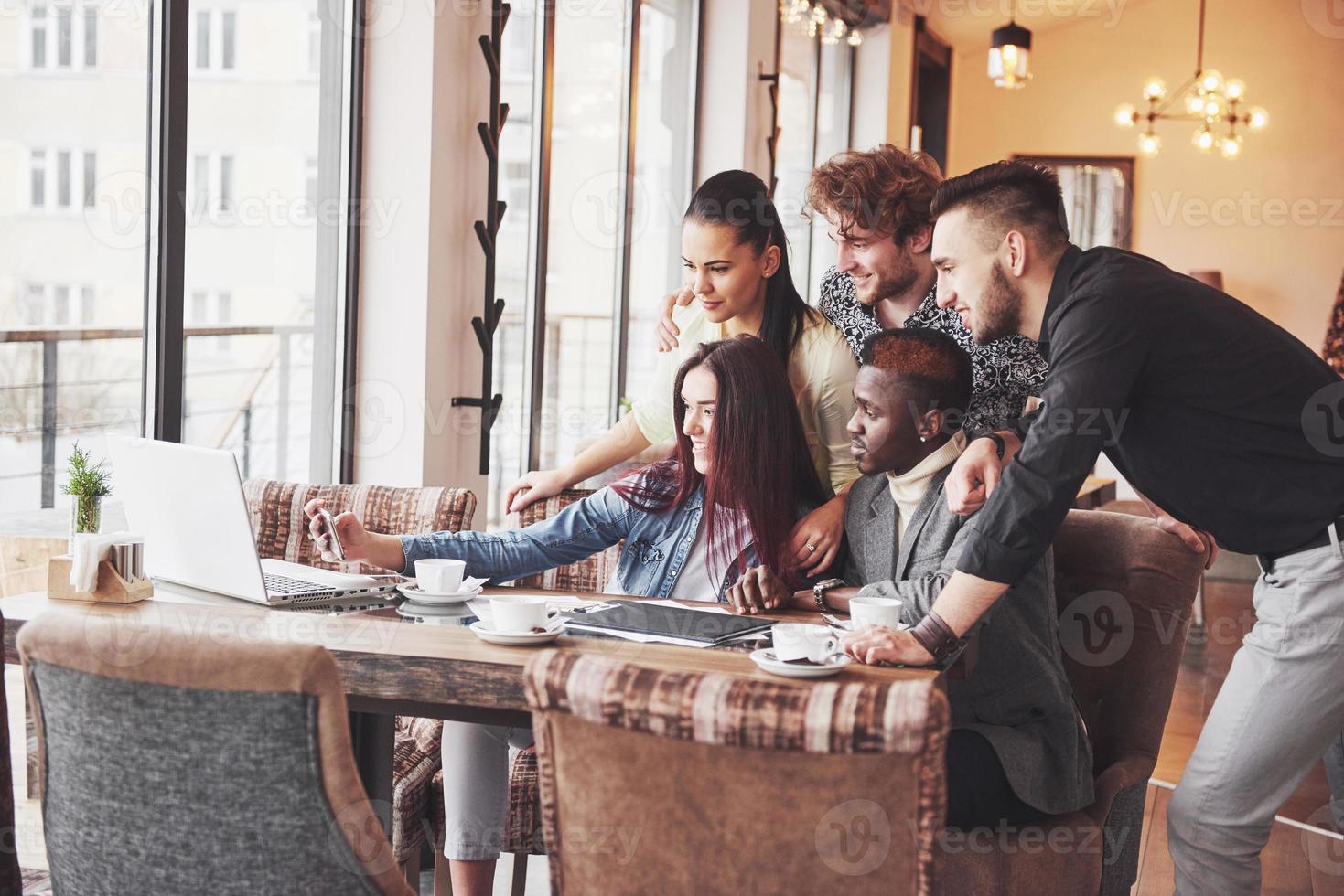 Friends having fun and making selfie at restaurant.Two boys and four girls drinking beer and eating pizza with fresh salad together. Boy with cap making selfie with his phone. All wear casual clothes photo