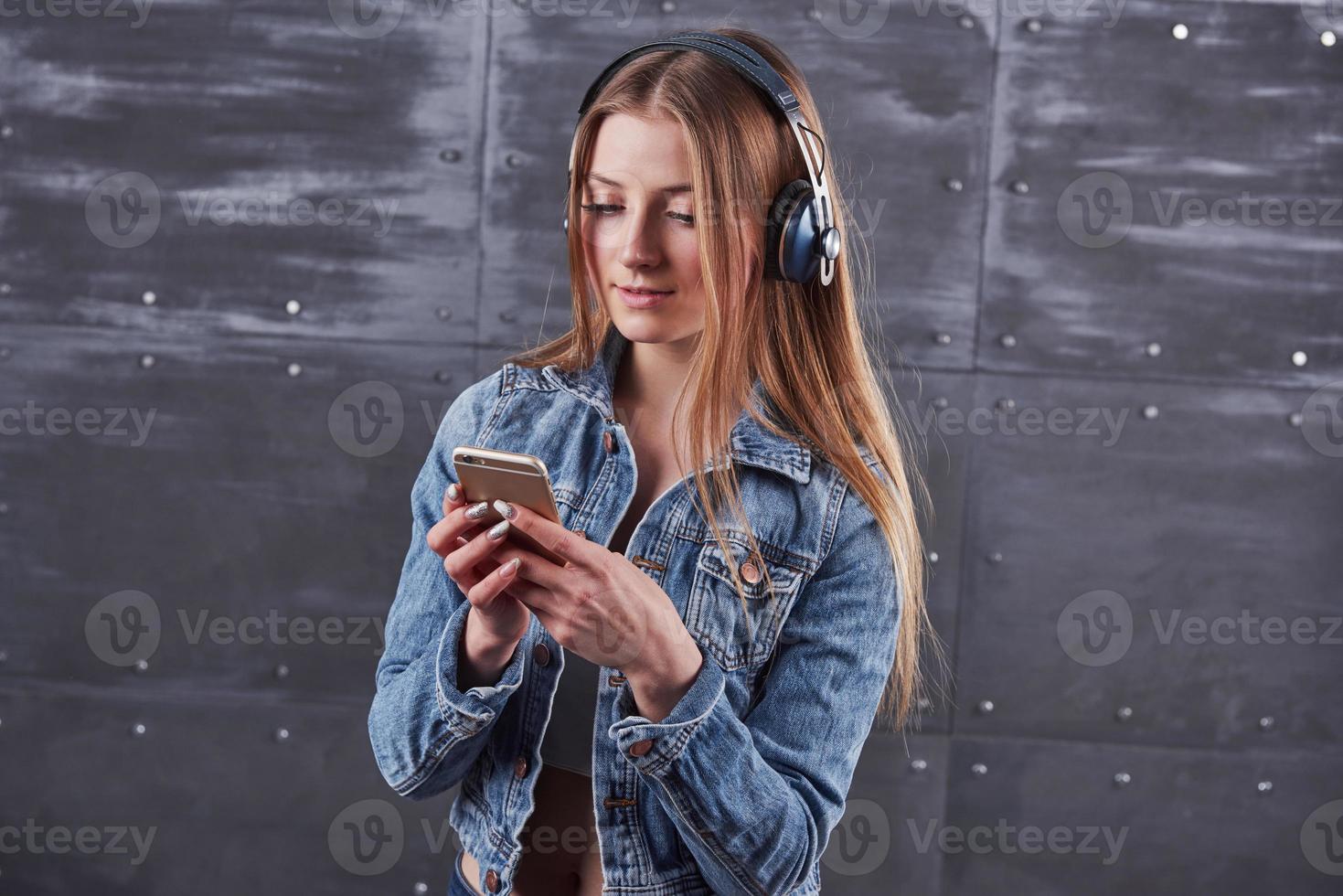 moda, ropa, concepto de personas. atractiva joven sexy con chaqueta de jeans. chica está posando en el estudio escucha música en auriculares foto