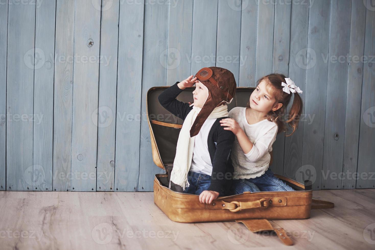 Happy kid in pilot hat and little girl playing with old suitcase. Childhood. Fantasy, imagination. Travel concept photo