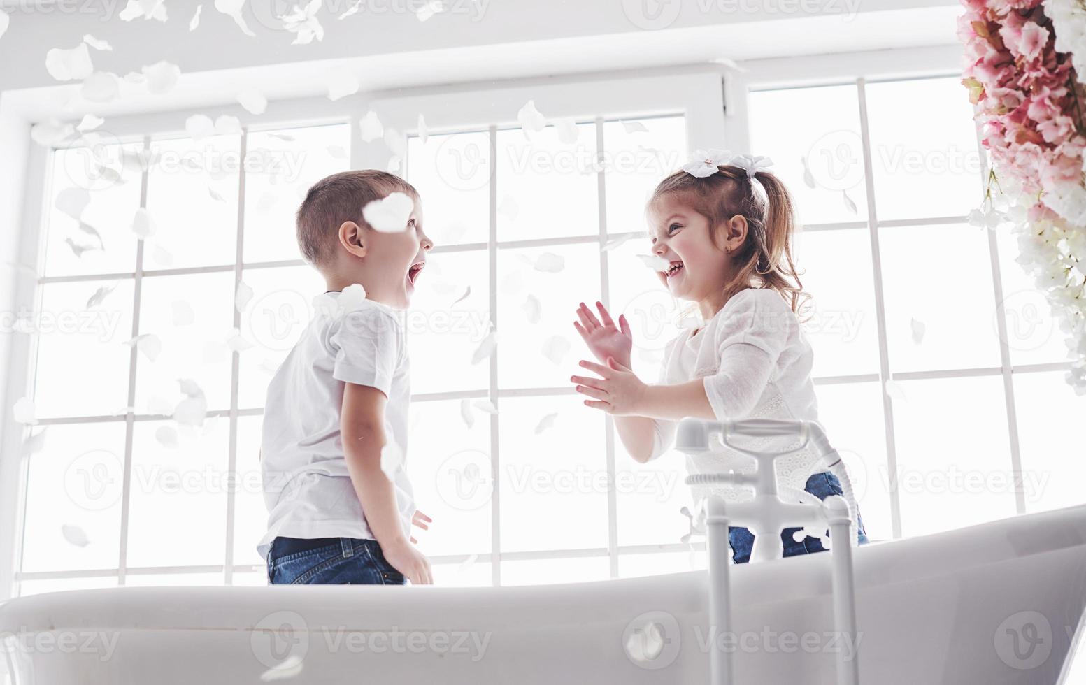 niño jugando con pétalos de rosa en el baño de su casa. niña y niño adulando diversión y alegría juntos. el concepto de infancia y la realización de sueños, fantasía, imaginación foto