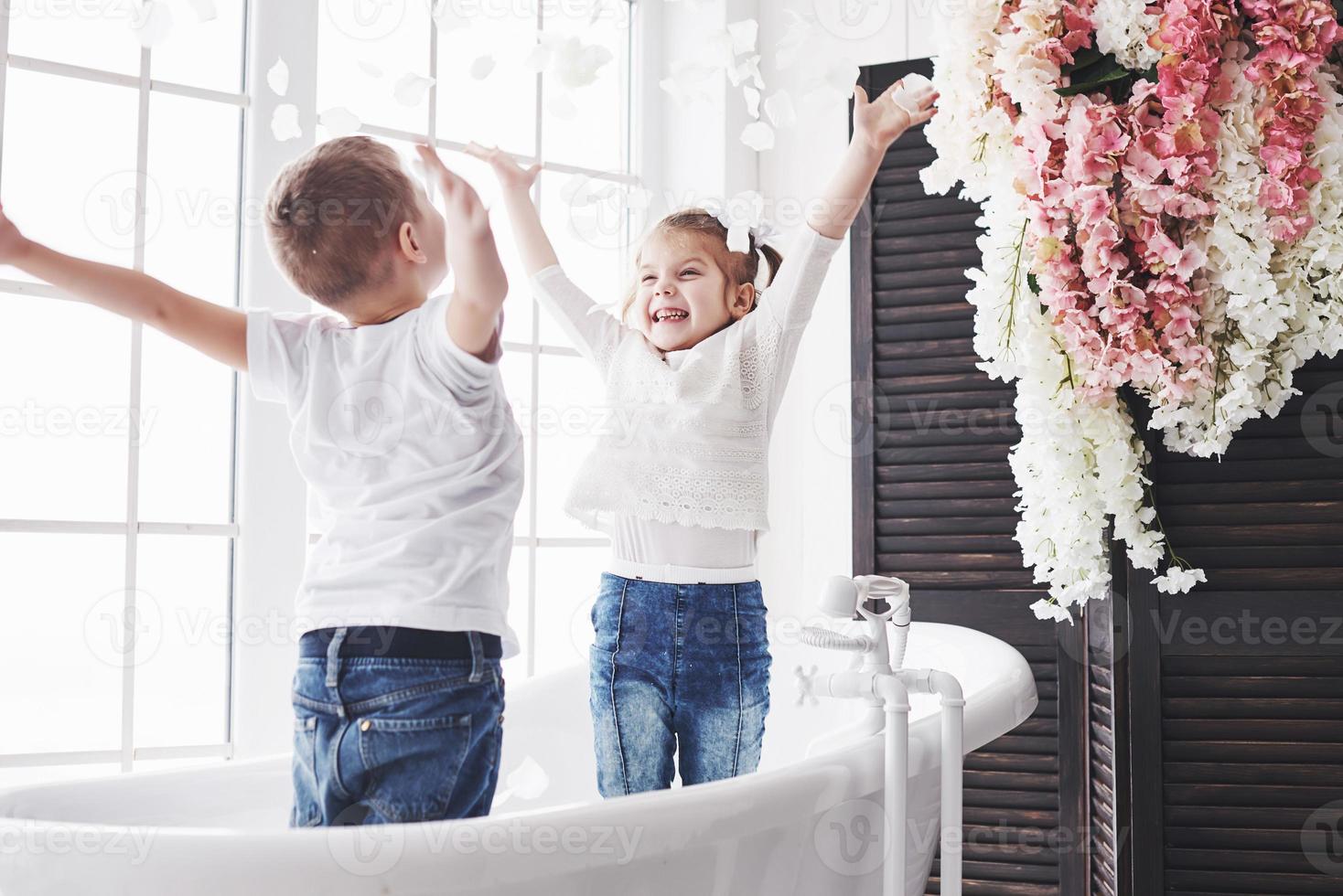 niño jugando con pétalos de rosa en el baño de su casa. niña y niño adulando diversión y alegría juntos. el concepto de infancia y la realización de sueños, fantasía, imaginación foto