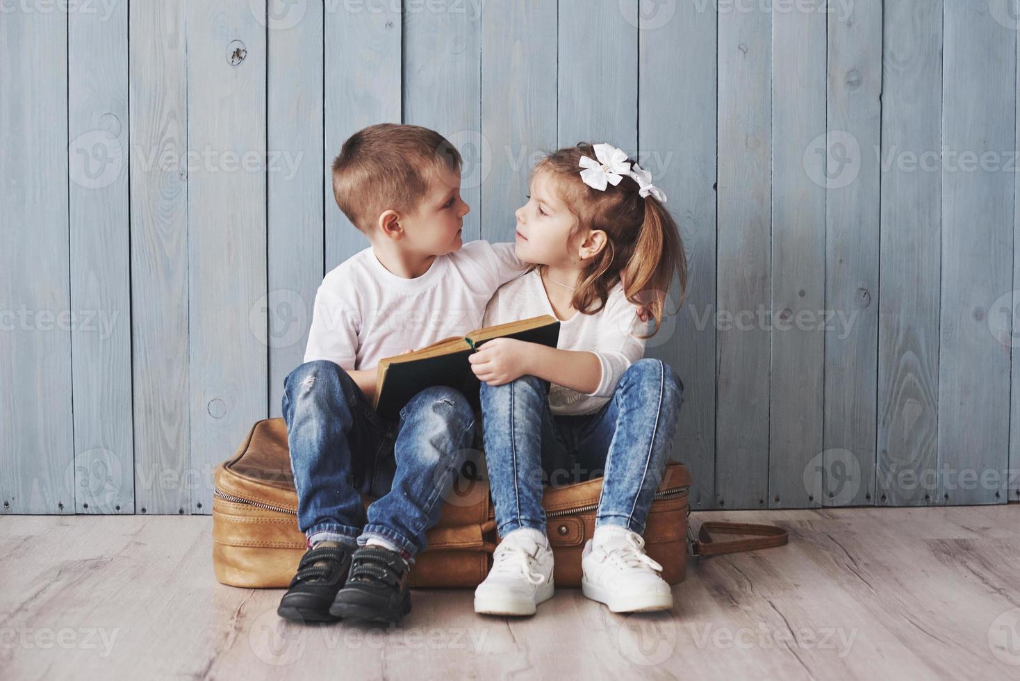 listo para grandes viajes. feliz niña y niño leyendo un libro interesante con un maletín grande y sonriendo. concepto de viaje, libertad e imaginación. foto